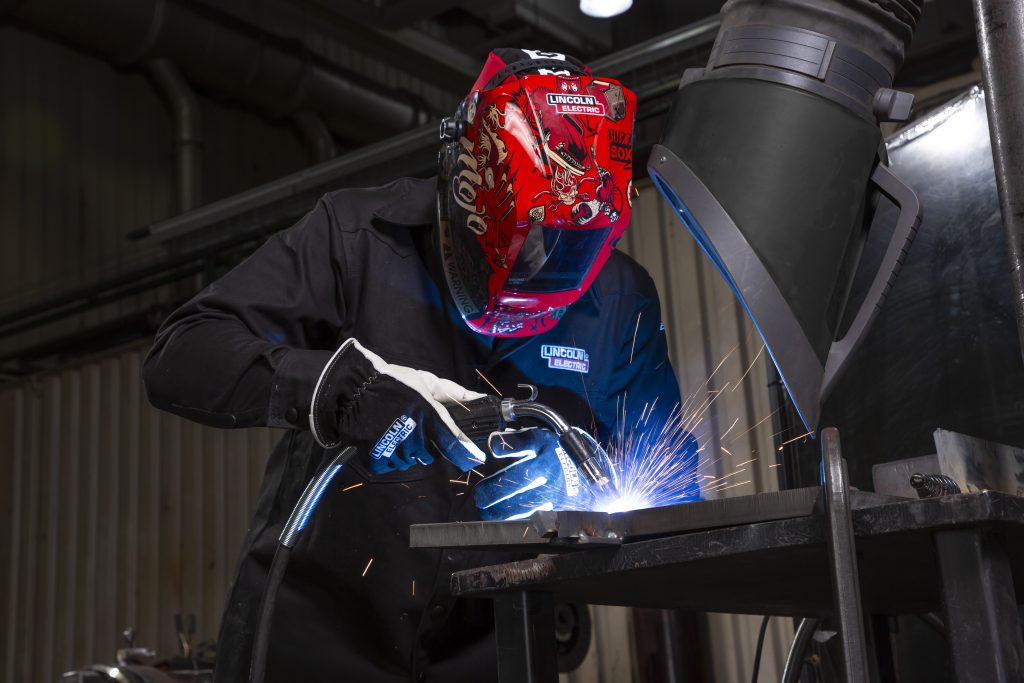 MIG Welding with a Magnum Pro 250A MIG gun. Welding gear includes Viking 3350 Mojo auto-darkening helmet, Black FR welding shirt and welder's driving gloves. Prism Wall Mount fume extraction arm also in use.
